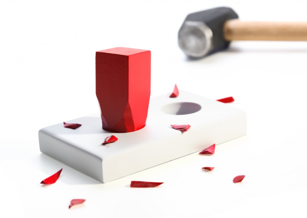 A square red peg hammered into a round hole surrounded by small pieces of the peg. Hammer in background. On a white background. Selective focus. Metaphor for a misfit, incompatibility. Check out my lightbox